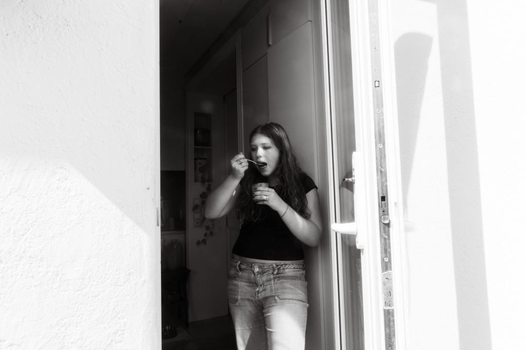 Kvinne spiser iskrem ved inngangsdøren i svart-hvitt bilde.