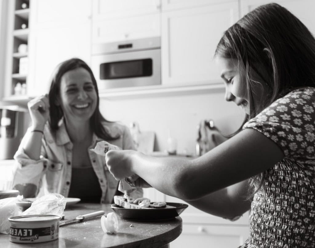 Kvinne smiler mens hun lager mat, mens den andre forbereder ingredienser.